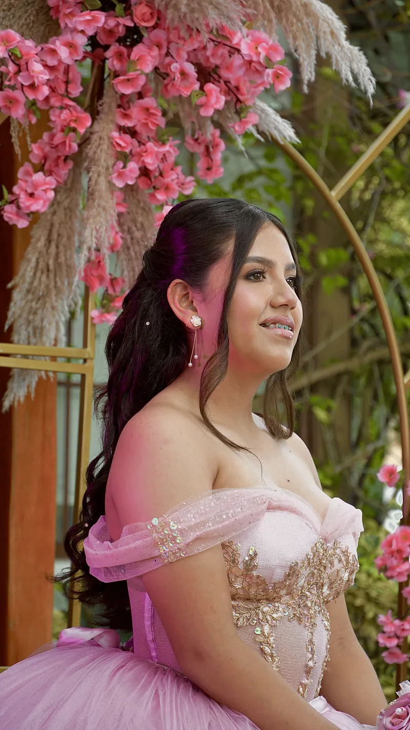 Quinceañera de perfil con vestido rosa bajo flores de cerezo